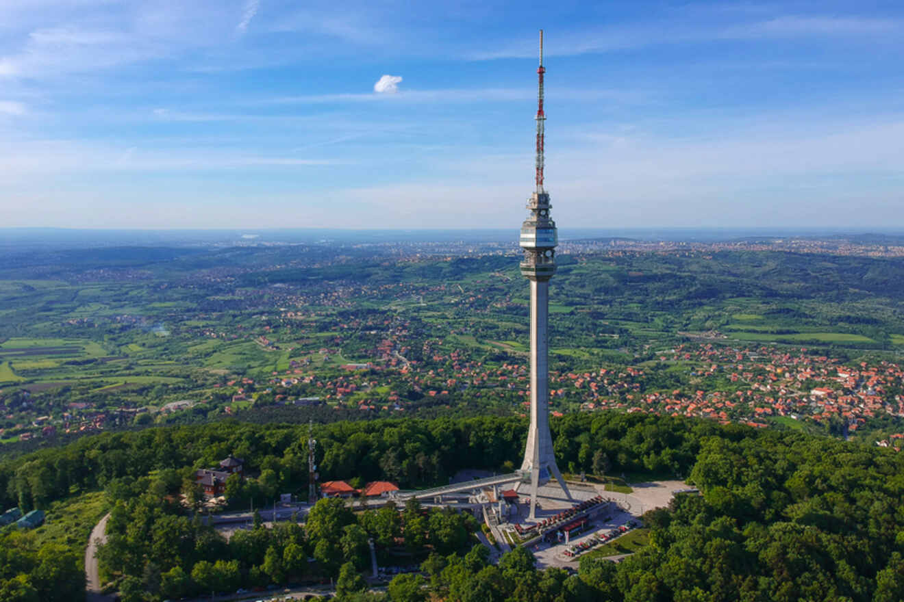 Aerial view of Avala Tower in Belgrade, a tall communications tower standing isolated on a green landscape with the city skyline in the far distance