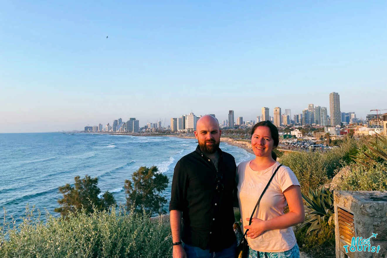 The writer and her partner standing together with a panoramic view of the Tel Aviv coastline in the background, showcasing the city's urban beachfront
