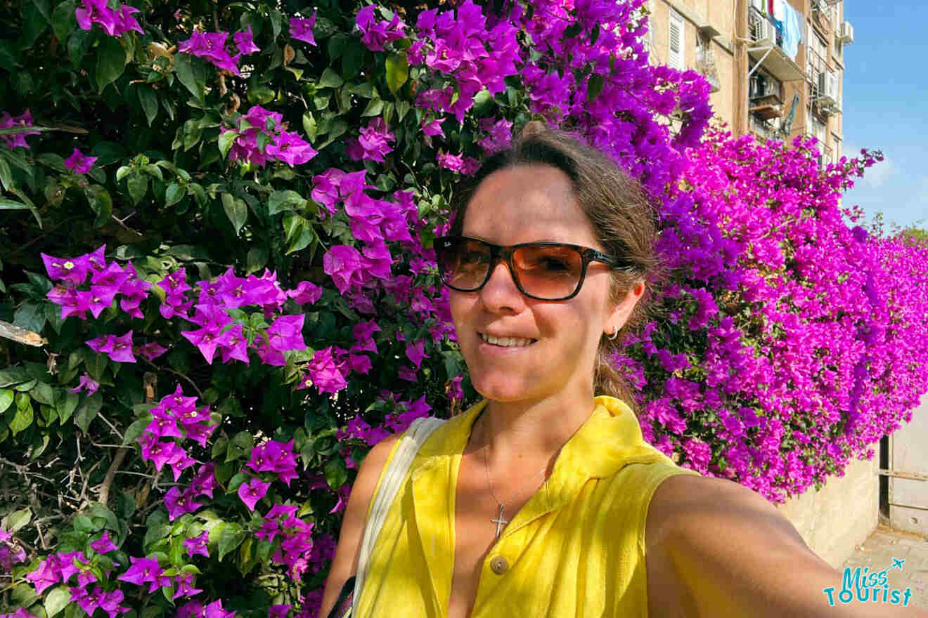 The writer of the post takes a selfie with a lush bougainvillea in full bloom in the streets of Tel Aviv