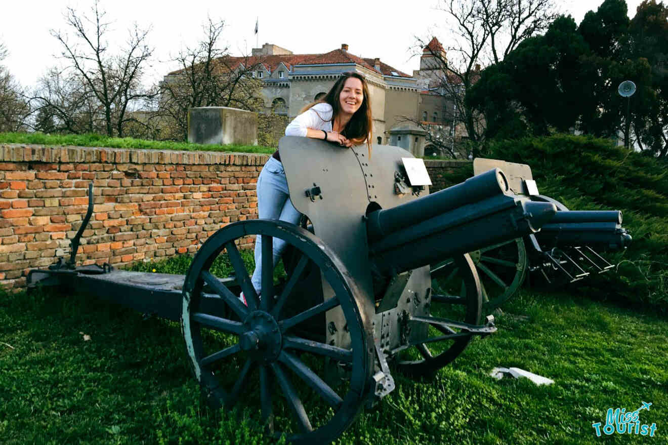 The writer of the post smiling while leaning on a historic cannon at Kalemegdan Park with the old fortress in the background