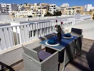 A hotel balcony dining area set for two, with a view of urban buildings under a clear sky.