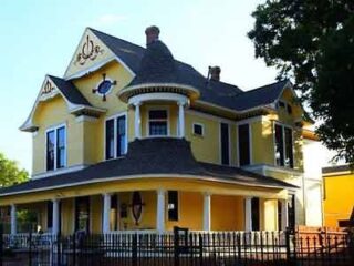 A charming yellow Victorian house with ornate detailing, a wrap-around porch, and a welcoming feel, set against a clear blue sky.