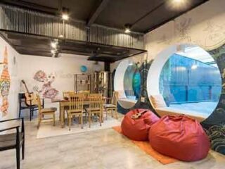 Chic and modern hostel common area with a unique circular window looking into the pool, comfortable red bean bags, and eclectic wall art, creating a trendy and welcoming social space.