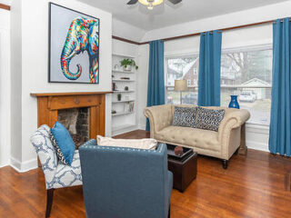 Inviting living room with vibrant elephant art above the fireplace, a beige tufted sofa, blue drapes, and hardwood floors
