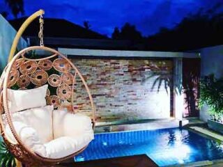 An intimate villa pool at night, illuminated by soft pool lights with a stylish rattan hanging chair in the foreground, offering a luxurious private retreat experience.