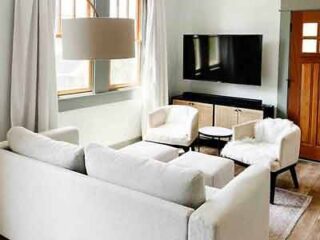 A contemporary hotel living room with white sofas, elegant light fixtures, and a clean, minimalist design aesthetic.