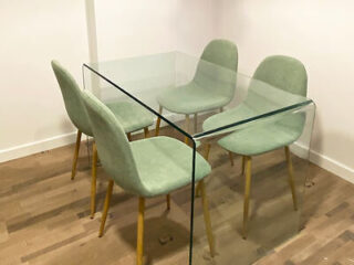 A minimalist dining area with a modern flair, showcasing a clear glass table and four plush mint green chairs