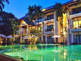 Resort-style hotel with a large swimming pool illuminated by green lights at dusk, featuring elegant colonial architecture and palm trees that enhance the tranquil atmosphere.