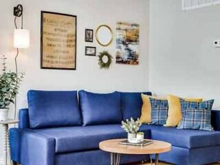 Modern living room featuring a vibrant blue sofa with yellow and plaid pillows, a round wooden coffee table, and eclectic wall decor for a cozy, contemporary feel.