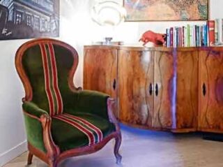 A vibrant corner of Art'To hotel with a vintage green and red striped armchair, a wooden cabinet with colorful door fronts, topped with books and a decorative red bull sculpture.