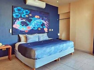 Contemporary bedroom featuring a large bed with blue bedding and a colorful abstract painting above, in a room with minimalist decor.