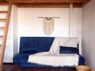 A simple and cozy loft space with a blue futon sofa, white throw, and a rustic wall hanging, exuding a casual charm.