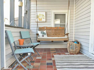 Quaint porch with a wooden swing bench, blue chairs, and a striped rug