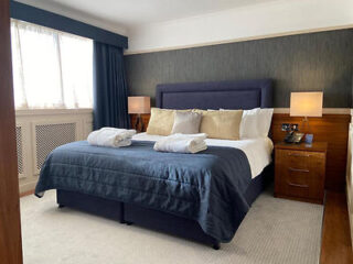 A stylish bedroom featuring a large blue bed with gold and white pillows, bedside lamps