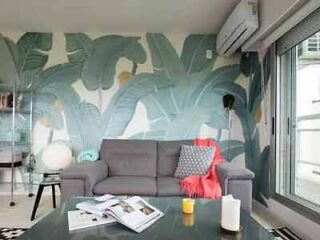 A contemporary living room with a stylish botanical mural, gray sofa, and vibrant orange throw, creating a fresh and trendy atmosphere.