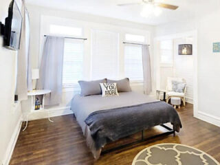 Bright bedroom featuring a dark wood floor, gray bedding with a 'LOVE YOU MORE' pillow, and a round patterned area rug