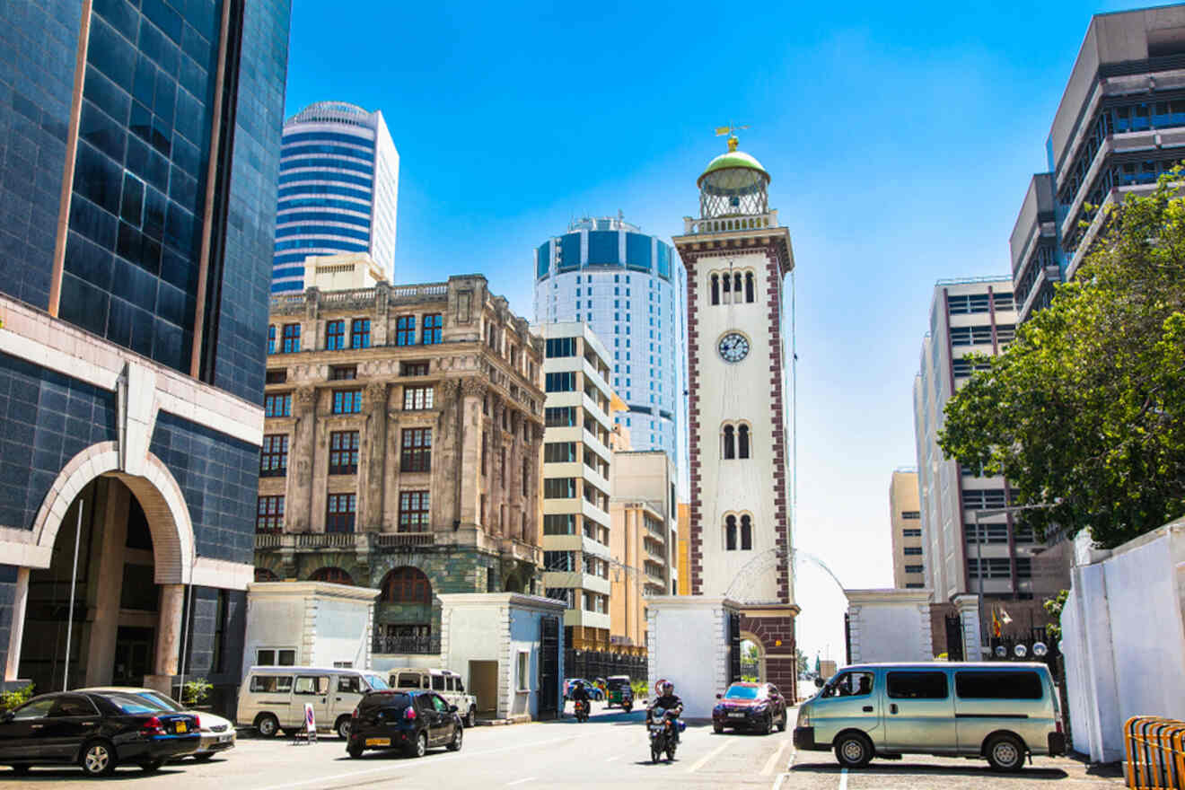 A bustling street scene in Colombo with a blend of modern and colonial architecture, featuring a prominent clock tower standing against a backdrop of high-rise buildings and clear blue skies.