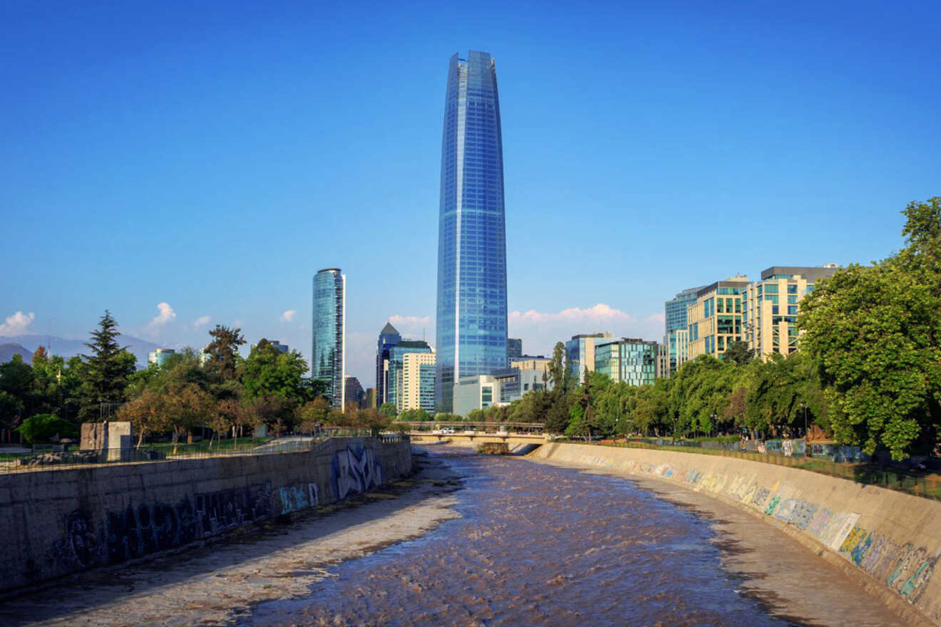 Sky Costanera Tower dominating the Santiago skyline beside the Mapocho River, with lush greenery and a clear blue sky