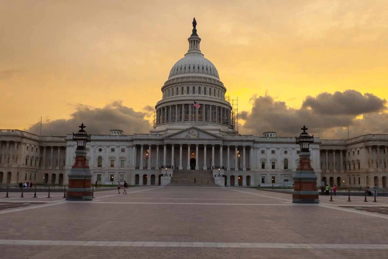 The United States Capitol Building at dusk, with the sun casting a warm glow on the iconic facade and steps, and a few people visible in the spacious plaza.