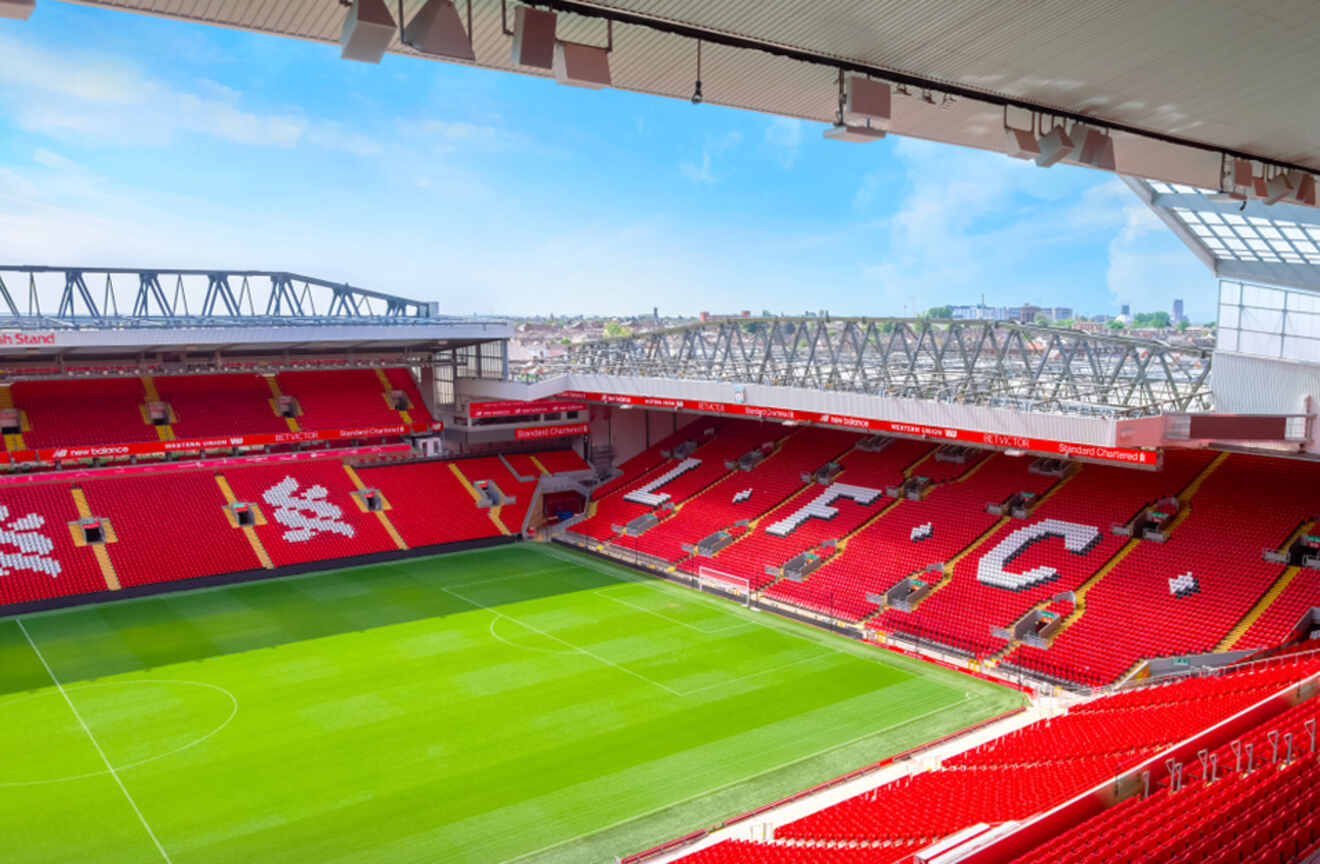 The iconic Anfield Stadium, home of Liverpool Football Club, with its vast, empty red seating and pitch, awaiting fans and players on a sunny day.