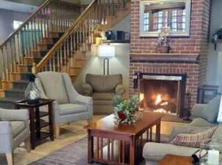 A traditional living room with a brick fireplace, wooden staircase, and comfortable beige seating, exuding a warm and homely feel.