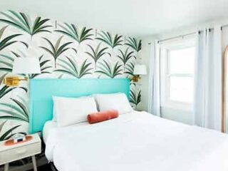 The Royal Palms Motel room featuring a relaxed setting with tropical wallpaper and a bright teal bed headboard.