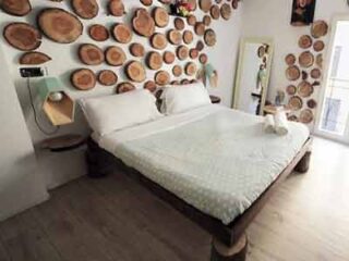 A bedroom with a unique wall decorated with wooden slices, a double bed, and minimalist furniture, for a nature-inspired restful retreat.