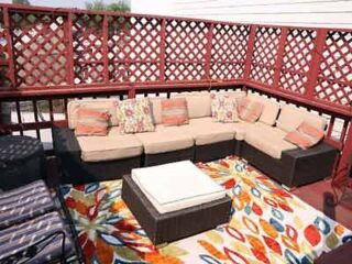 A cozy rooftop patio furnished with a large sectional sofa adorned with colorful pillows, set against a red lattice backdrop for a casual outdoor setting.