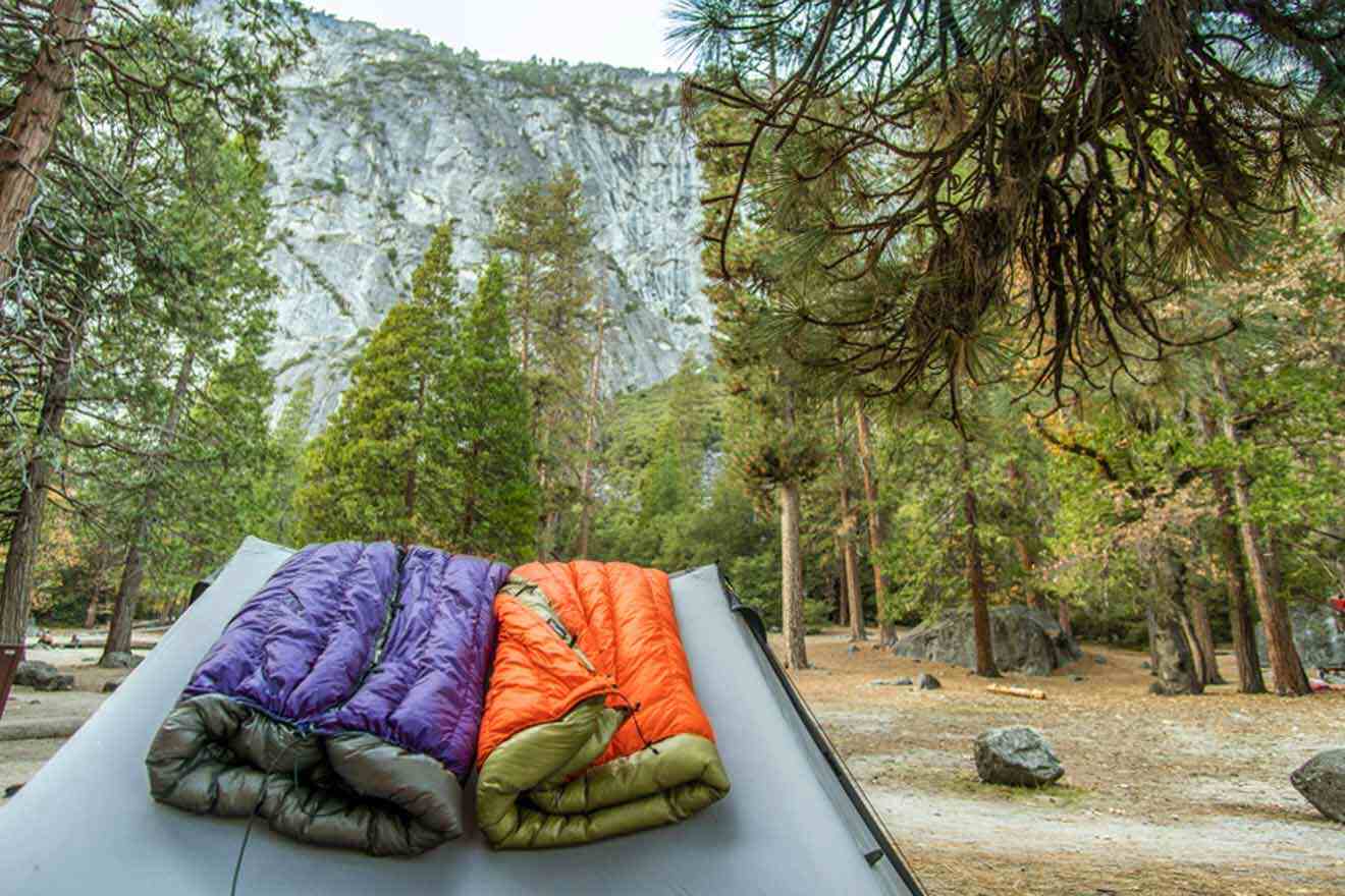 Colorful sleeping bags on the roof of a vehicle with a view of a pine forest and granite cliffs at a Yosemite campsite.