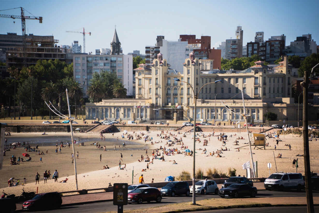 Busy beach scene in Montevideo with sunbathers dotting the sandy shore in front of an elegant, historic building, while the city's architecture rises in the background, creating a contrast between leisure and urban development