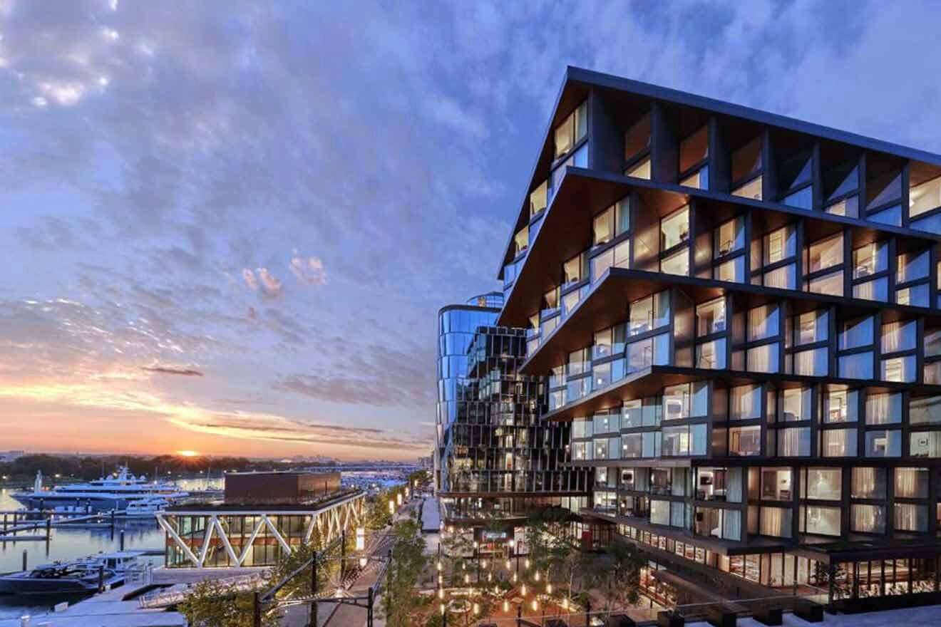 A modern architectural marvel at sunset, the building features distinctive geometric balconies with a view of the waterfront, highlighted by the warm glow of the setting sun.