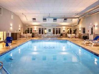 An indoor hotel swimming pool with evening lighting, enclosed within a spacious area with multiple seating options, ideal for relaxation.