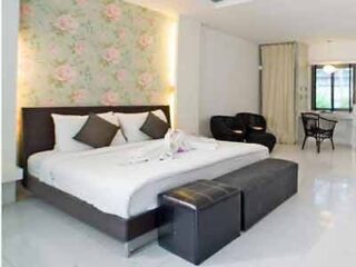 Elegant hotel room with a large bed and stylish brown headboard, soft floral wallpaper, and a comfortable seating area, reflecting a blend of modern and romantic design elements.