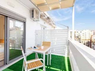 Private balcony with white railings, outdoor furniture, and artificial grass, offering a city view.