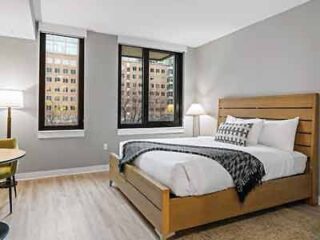A hotel room with a wooden bed, contemporary decor, and large windows offering a cityscape view, providing a sleek urban living experience.