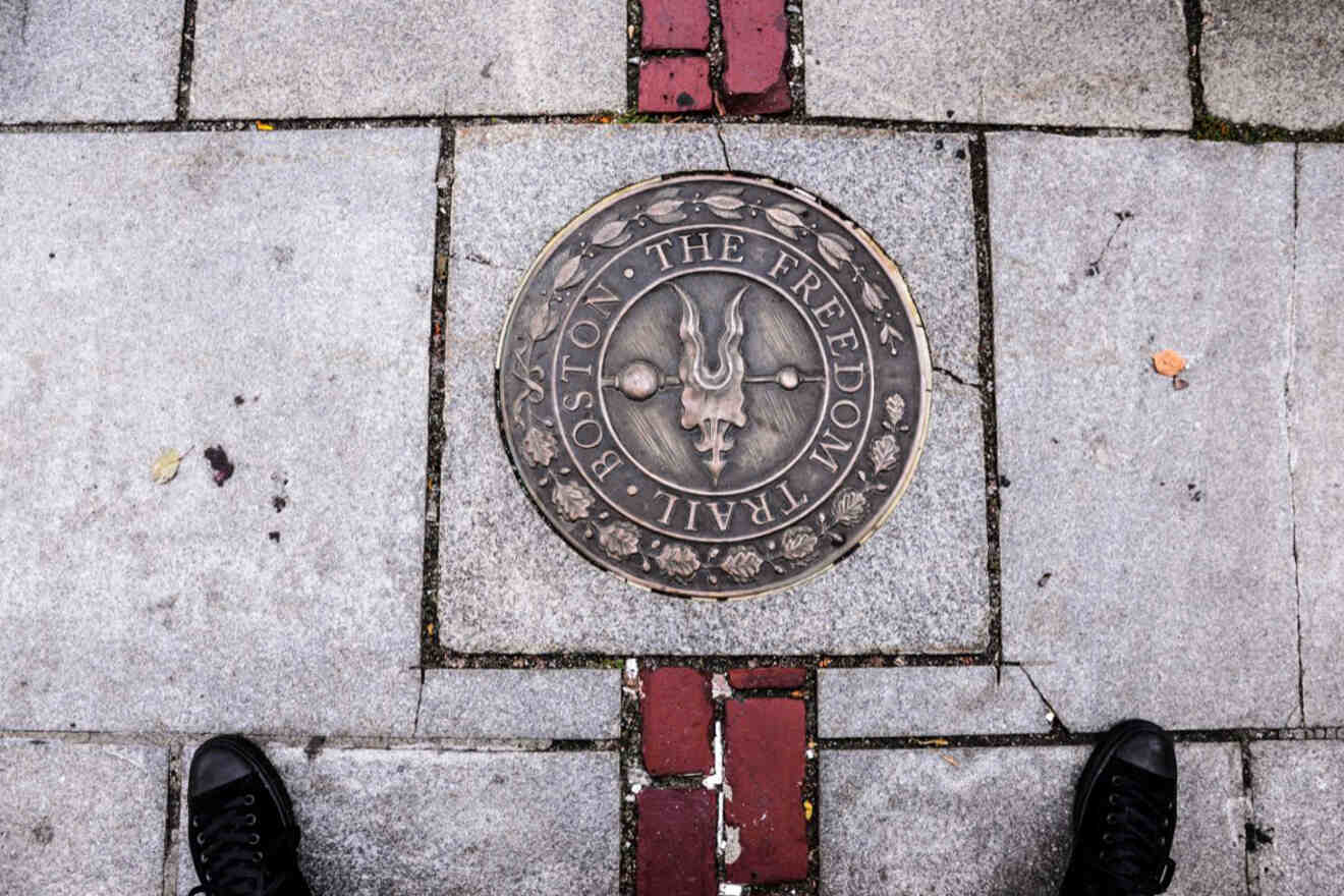 Close-up of the Boston Freedom Trail marker, a circular bronze medallion embedded in the pavement with intricate designs and inscriptions