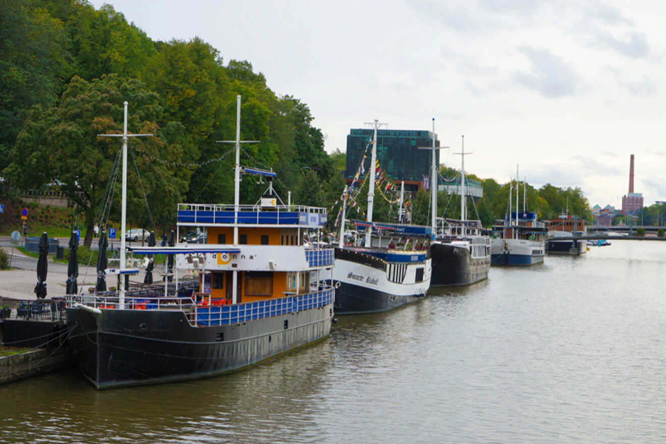 Boats moored along the Aura River in Turku, one transformed into a floating restaurant with patrons enjoying meals on deck