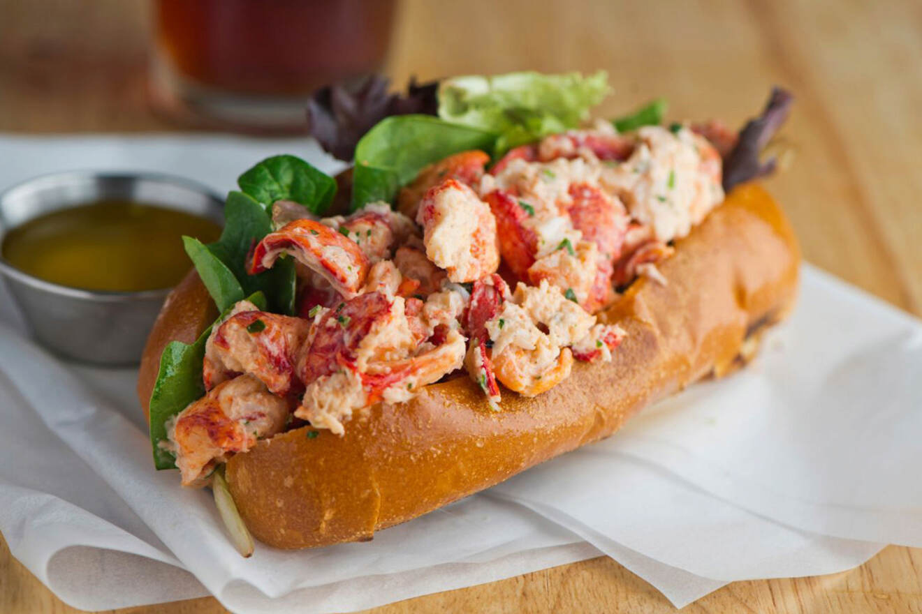 Fresh lobster roll on a plate with green leafy garnish, presented on a wooden table, a classic example of Boston's seafood cuisine
