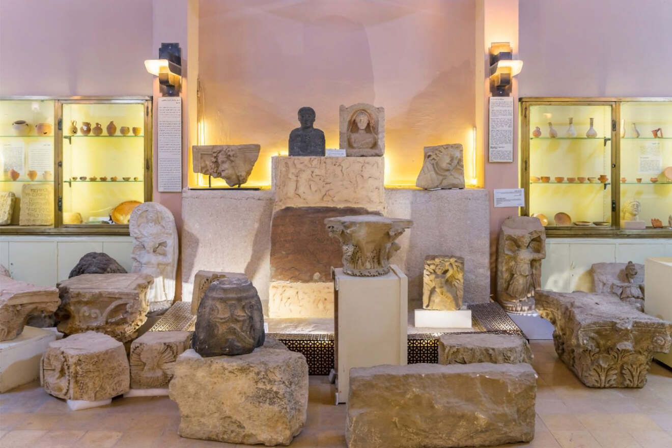 Interior of a museum display in Amman, Jordan, featuring an array of ancient artifacts, sculptures, and informational displays softly lit against peach-colored walls