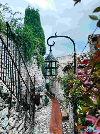 A picturesque cobblestone alley in Èze, France, with a vintage street lamp and lush greenery