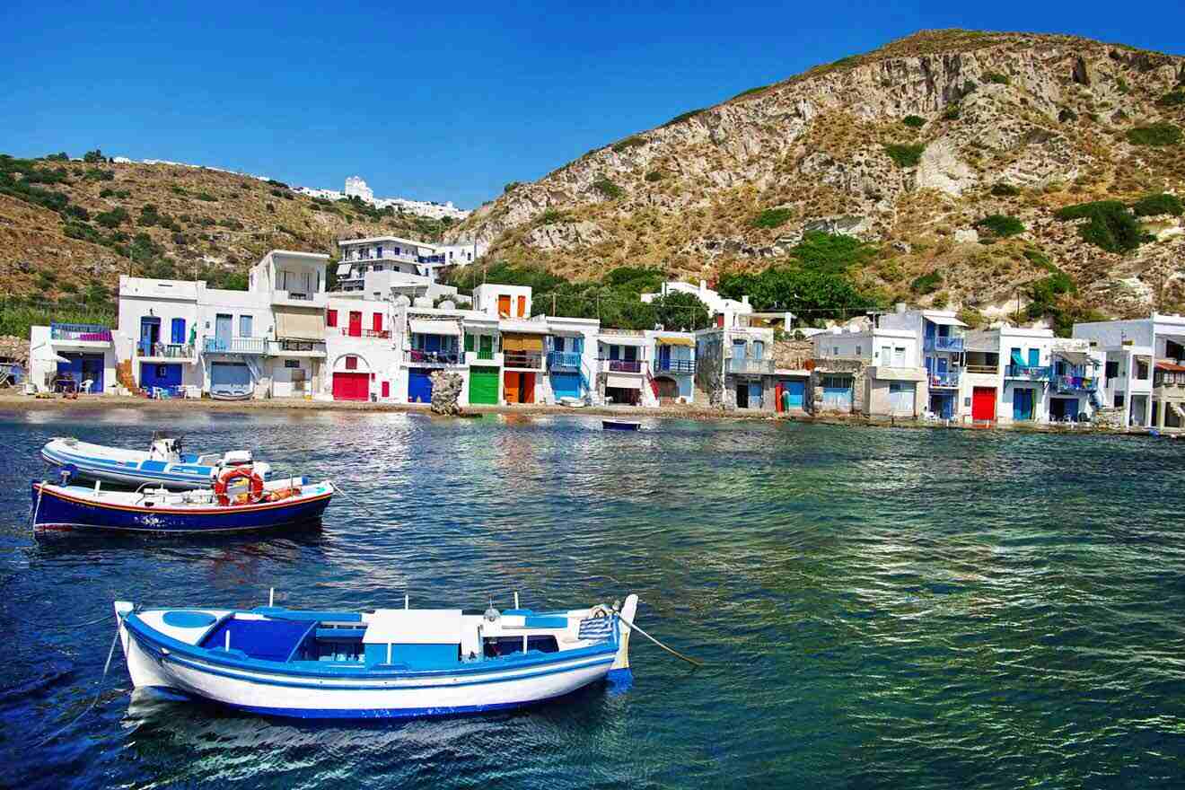 Colorful boathouses in the fishing village of Klima on Milos Island, with traditional boats moored in the clear blue water.