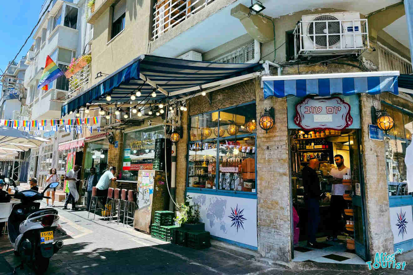 A sunny street view in the Neve Tzedek-Florentin district of Tel Aviv, with quaint shops, street flags, and a person entering a café