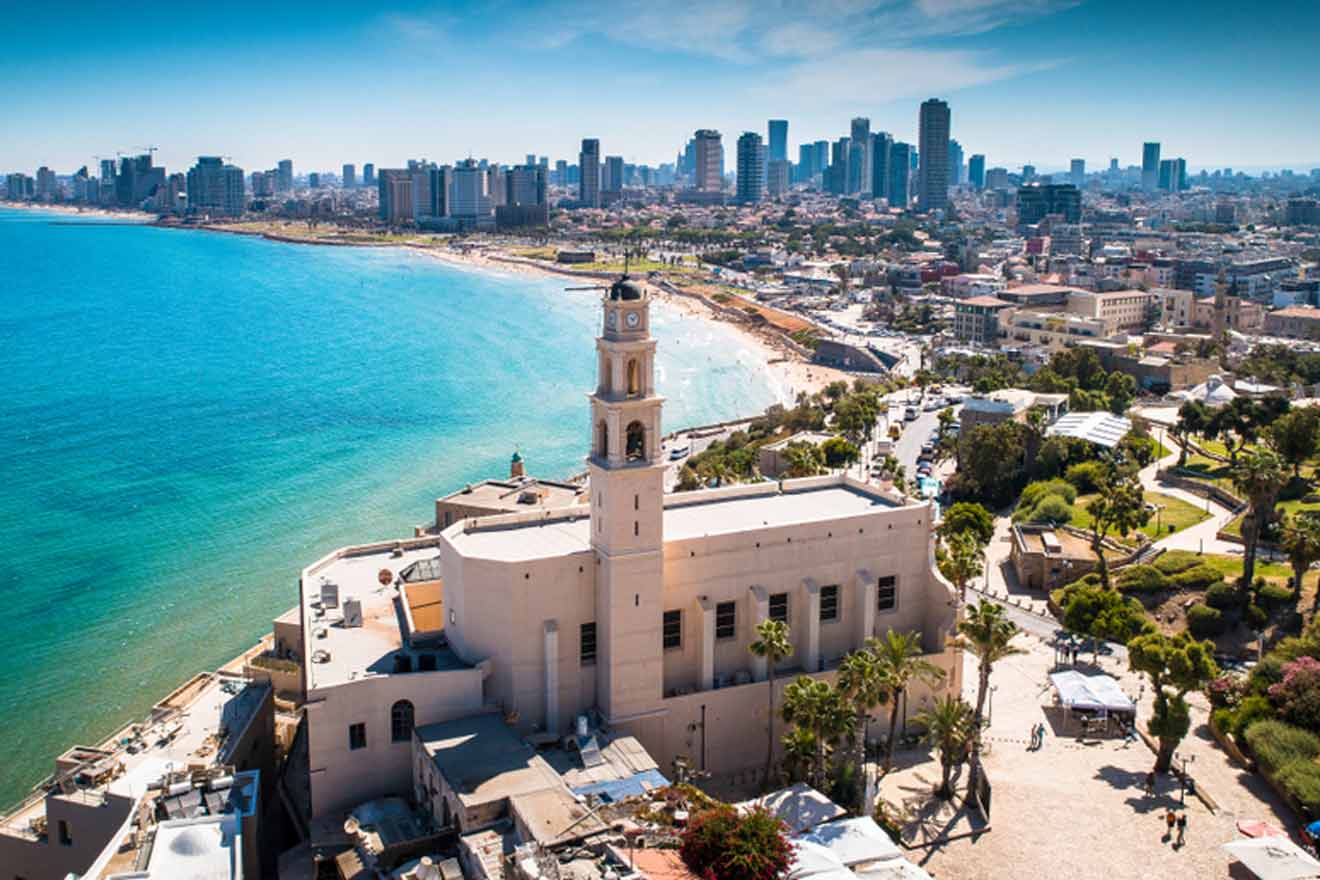 Aerial view of Tel Aviv coastline with a clear view of the Mediterranean Sea, sandy beaches, and the city skyline featuring modern architecture, with the prominent St. Peter's Church in the foreground.