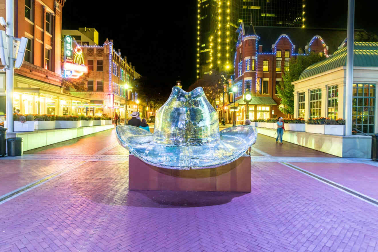 A dazzling ice sculpture of a cowboy hat creates a striking focal point in the vibrant nightlife of Fort Worth, surrounded by glowing lights and historical buildings, evoking the city's rich cultural tapestry and luxury accommodations