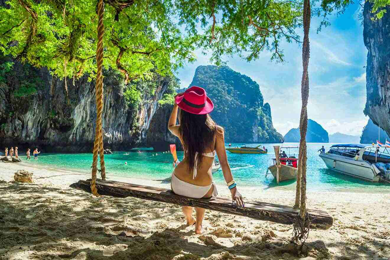 Woman in a white bikini and red hat sitting on a swing at Lao Lading island, with the stunning backdrop of clear turquoise waters, limestone cliffs, and anchored boats, capturing the essence of a tropical paradise adventure in Phuket.