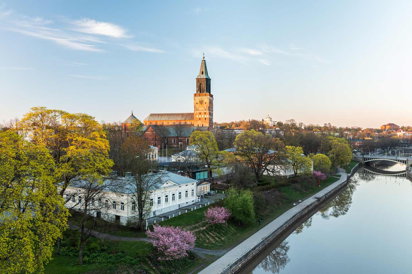 Sunset view of the Turku Cathedral by the Aura River in Finland, with blooming cherry trees along the riverbank and a clear blue sky