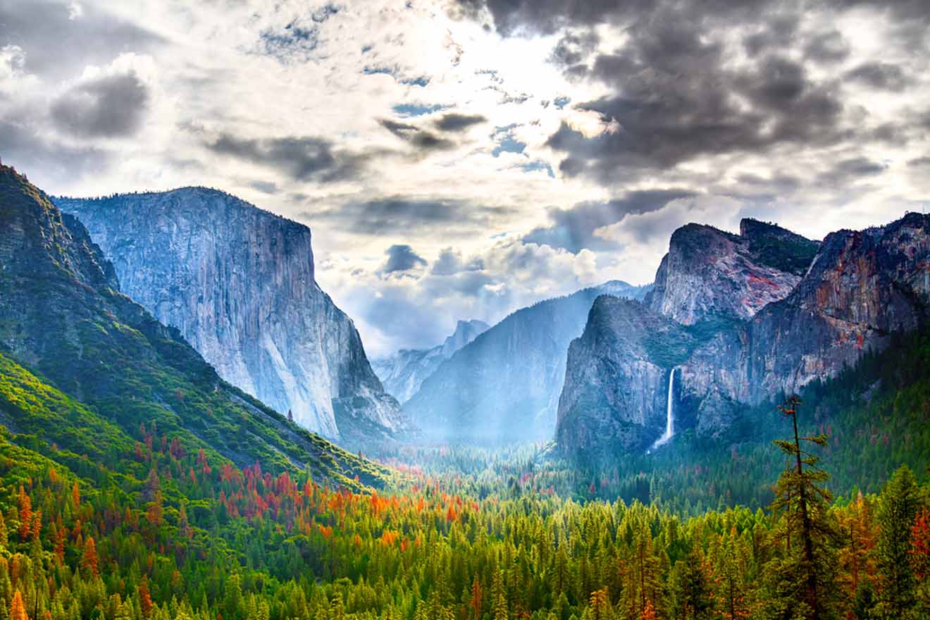 Majestic view of Yosemite Valley with El Capitan and Bridalveil Fall amidst a lush forest under a cloudy sky.
