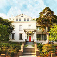 Historic Argos Inn with a neoclassical facade, red door, and surrounded by lush greenery under a clear sky.