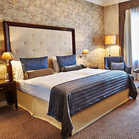 Elegant hotel room at Steigenberger Frankfurter Hof with a luxurious bed, plush blue throws, classic furniture, and warm lighting