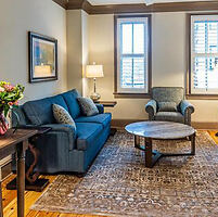 Cozy living area at the Andrew Pinckney Inn with a navy blue sofa, a comfortable armchair, a wooden coffee table, and hardwood floors, creating a welcoming atmosphere